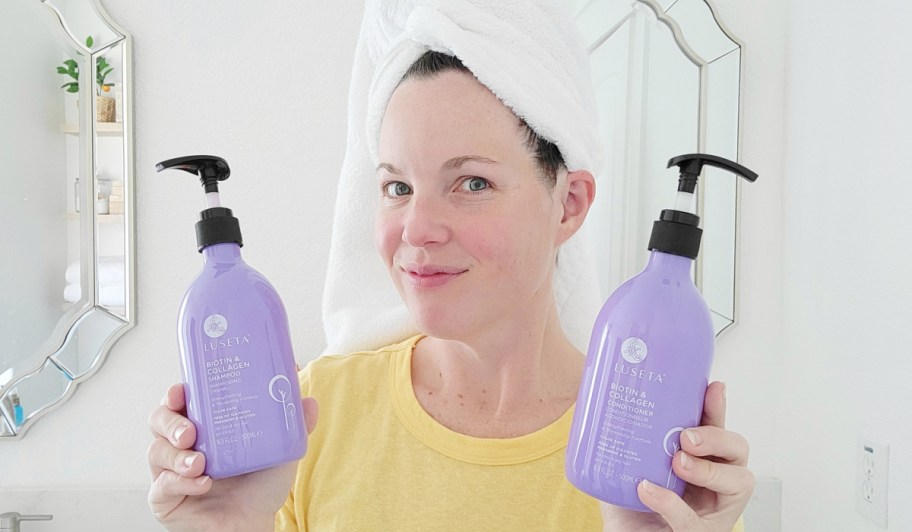 woman with towel on head holding purple shampoo & conditioner bottles
