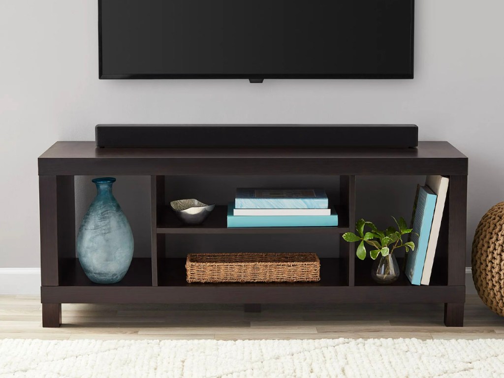 brown tv stand with vase and other items on shelves and tv hanging above