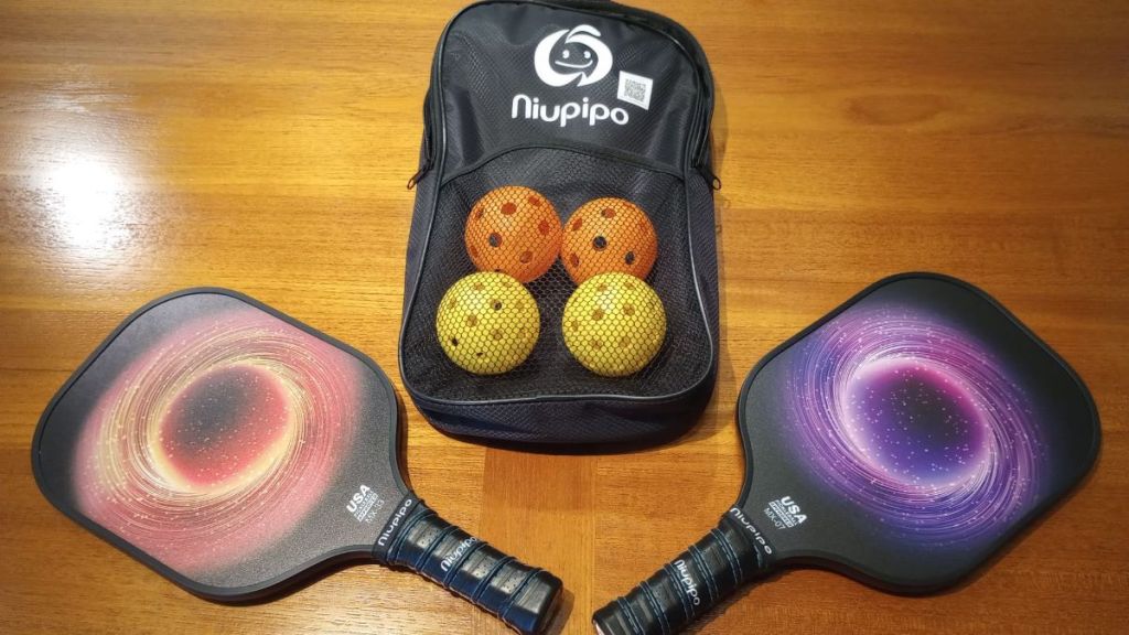 Two pickleball paddles by a bag that has four pickleballs in it