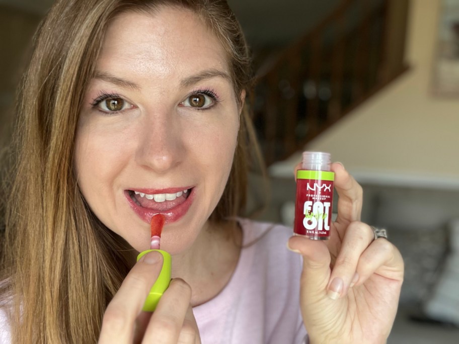 woman applying nyx fat lip oil and smiling at the camera