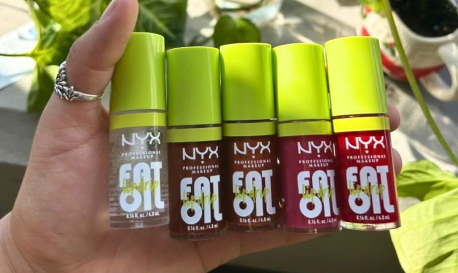a womans hand holding 5 tubes of nyx fat oil lip oil in various shades