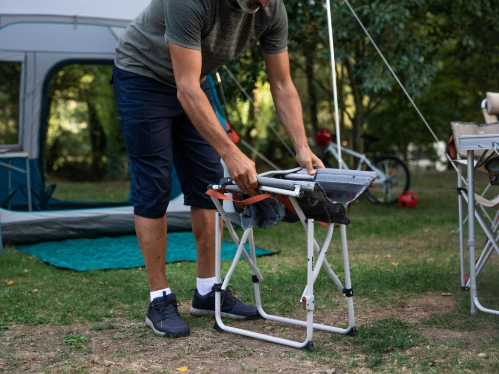 person folding Decathlon Quechua Director Folding Camping Chair at a camp site