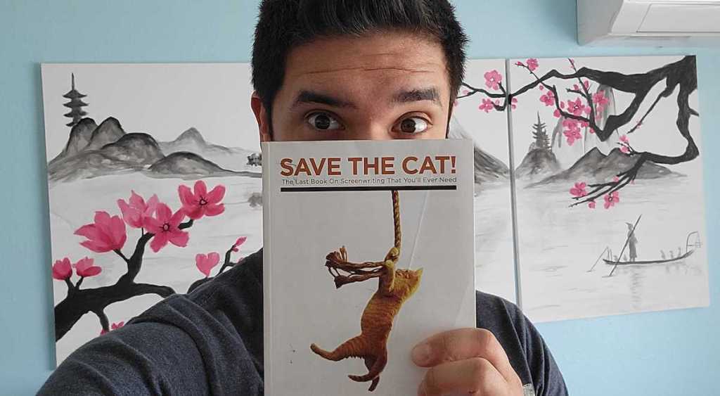 man holding up save the cat book in front of face