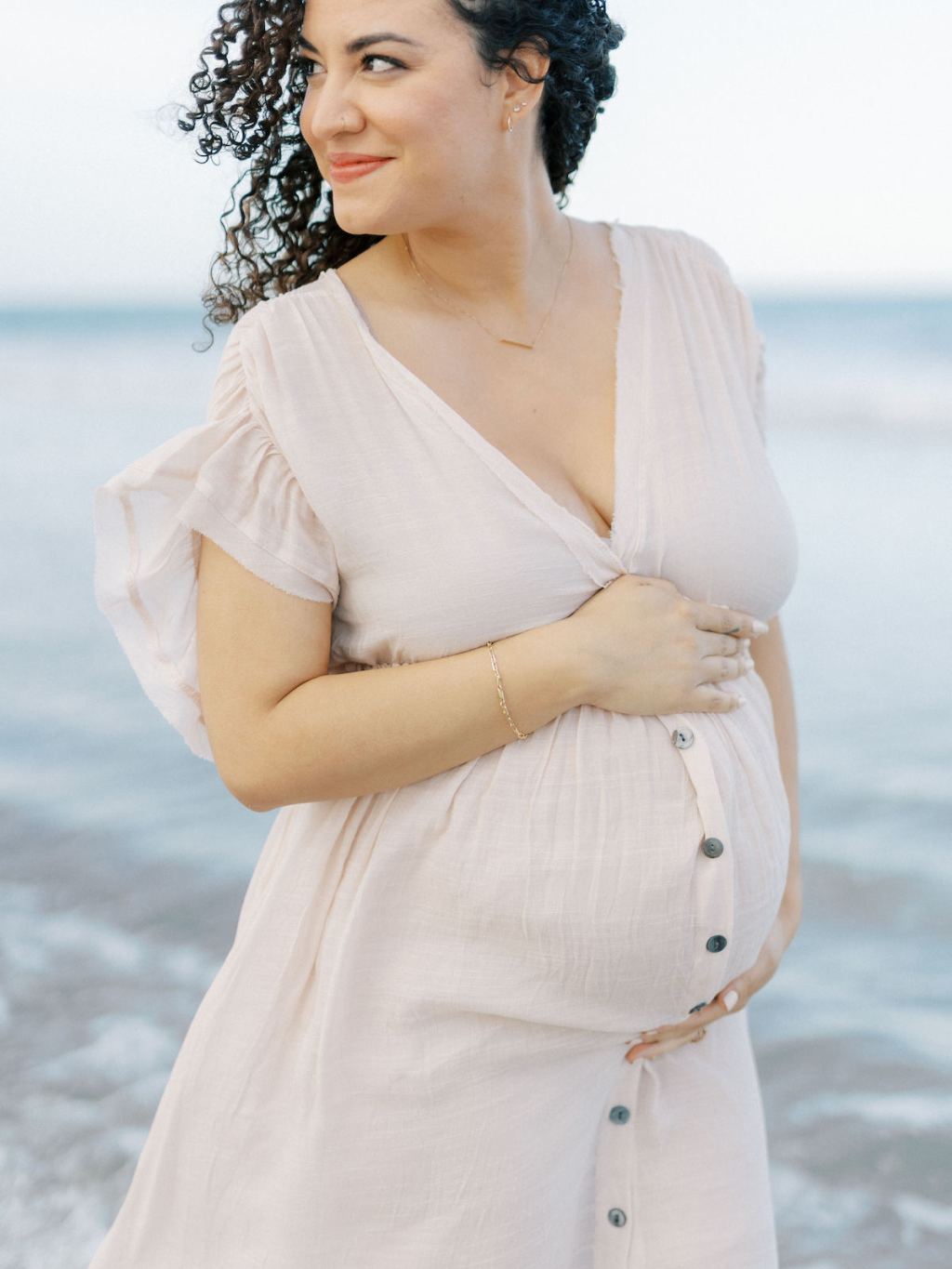 woman holding baby bump wearing flowy light pink dress on beach