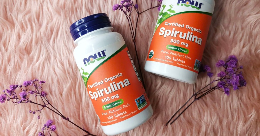 two bottles of spirulina tablets on pink furry rug with flowers