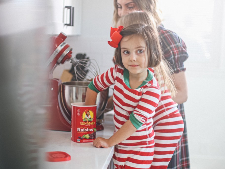 little girl wearing red and white striped pajamas sticking her hand in a sun maid raisins canister