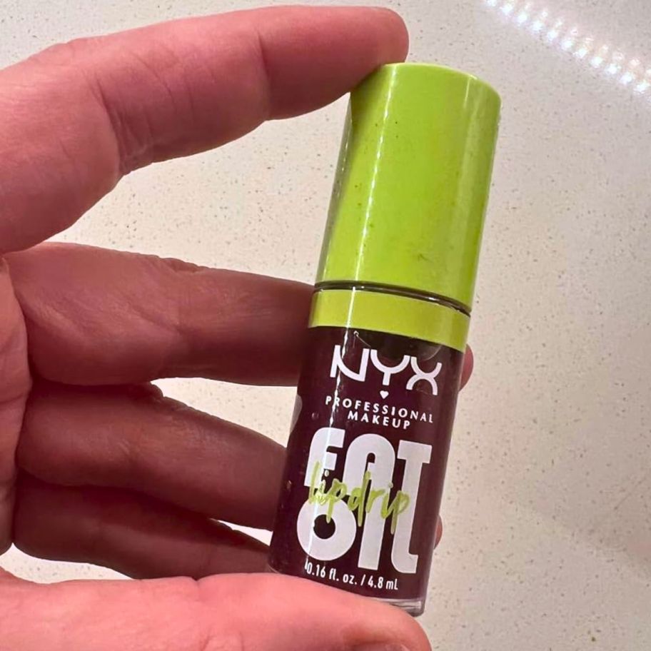a womans hand holding a tube of NYX fat oil lip oil