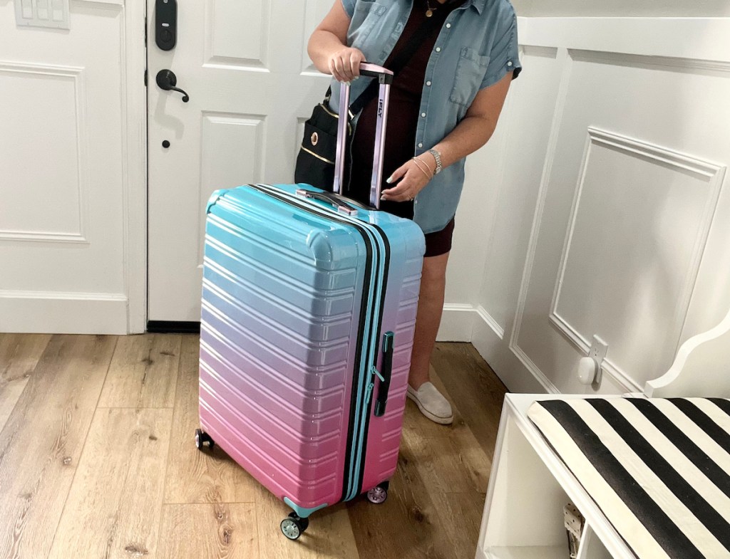 woman standing in foyer holding handle to colorful blue and pink luggage