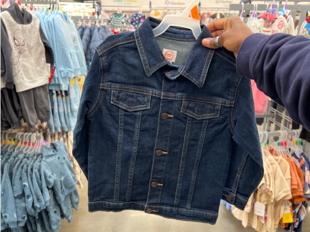 woman holdingg kids jean jacket at the store with clothing behind her