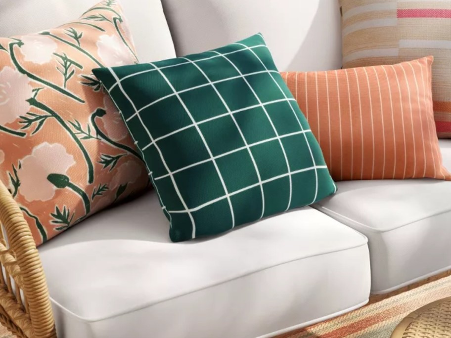 peach, green and white outdoor throw pillows on an outdoor wicker loveseat