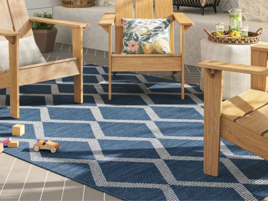 large blue and white diamond pattern outdoor rug with Adirondack style chairs around it