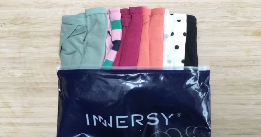 6 pairs of colorful women's underwear rolled up and sticking out of a bag that says 
