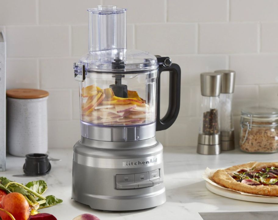 a food processor with sliced apples in the bowl sitting on a kitchen counter