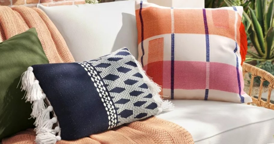 Navy and white geometric print outdoor pillow next to a pink, orange and navy plaid outdoor throw pillow