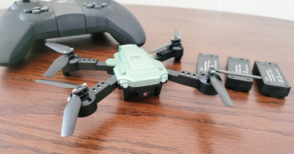 green mini drone with controller and batteries on table