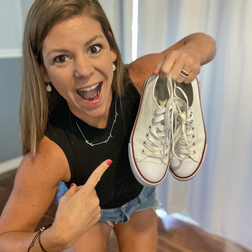 woman holding up and pointing to a pair of white canvas sneakers