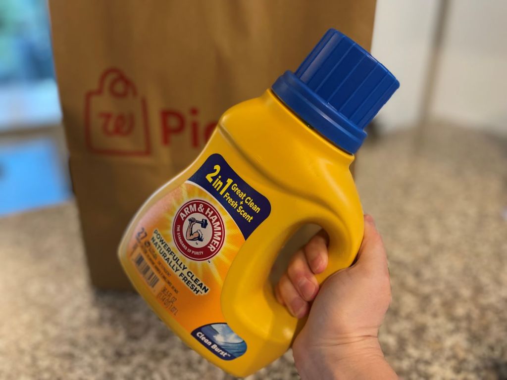 Hand holding a bottle of Arm & Hammer Laundry Detergent by a Walgreens bag