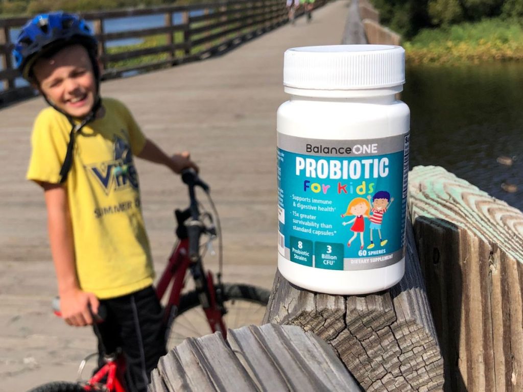 Child wearing bike gear in the background of a bottle of Balance One Kids Probiotic