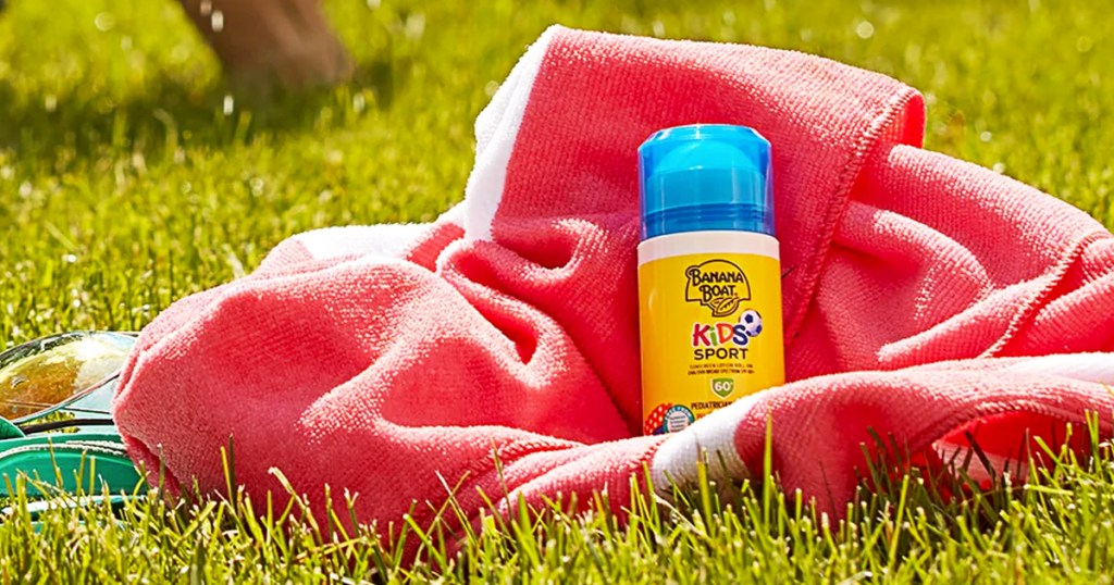 yellow tube of Banana Boat Kids Sport Roll-On Sunscreen sitting in grass on a pink towel