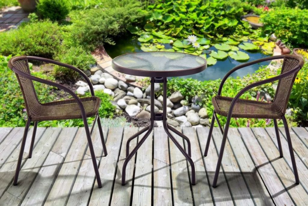 Two chairs and a table on a deck with a garden behind them