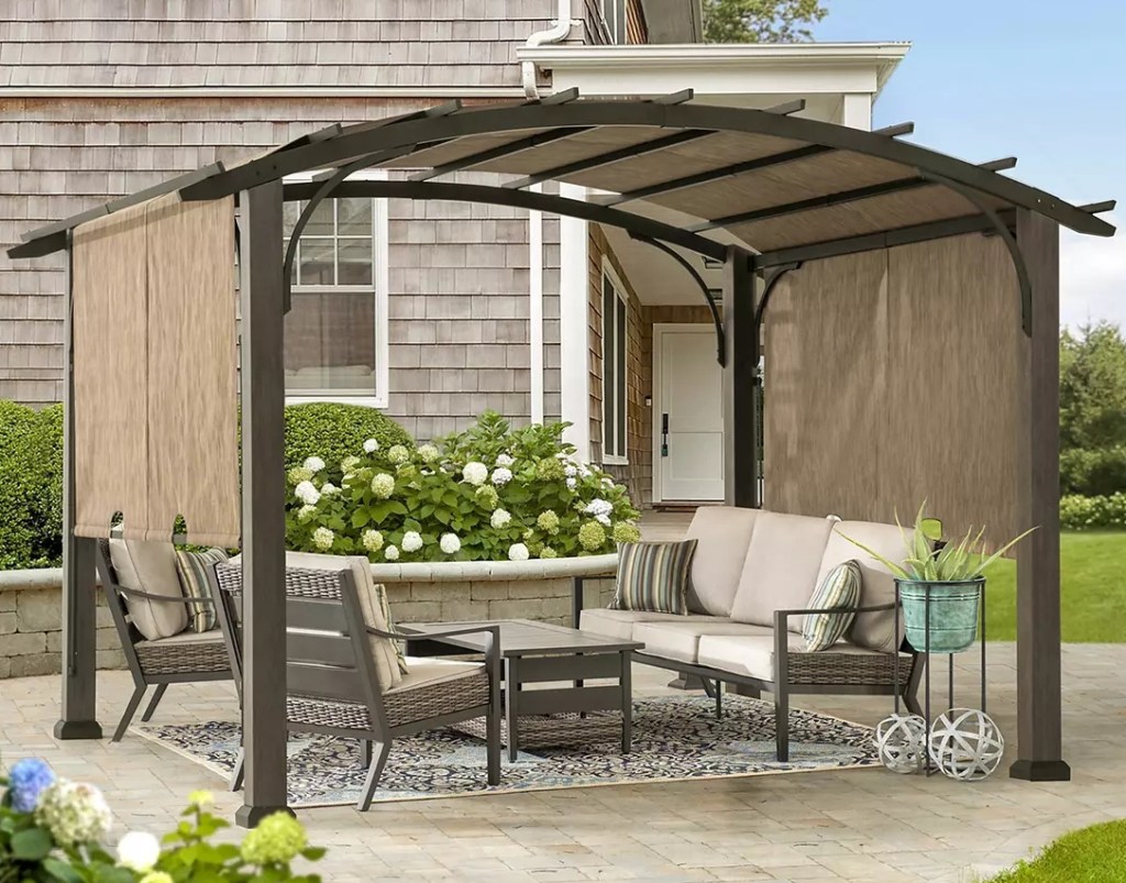 Brown steel pergola with tan canopy on it and patio furniture underneath it