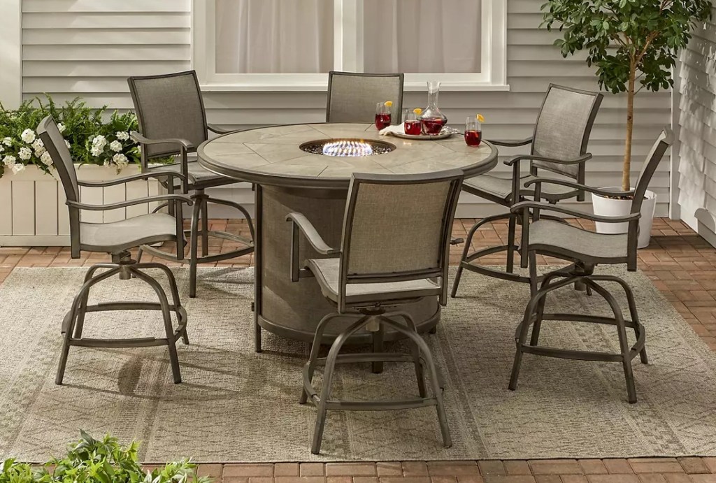 Tall patio dining set with chairs and a table that has a firepit in the middle
