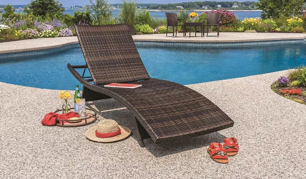 Wicker chaise lounge with a sun hat next to it sitting next to a pool