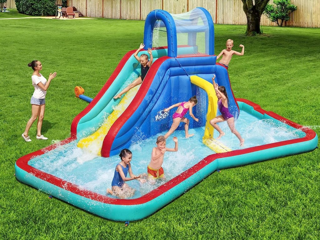 6 kids playing on Bestway H2OGO! Waterfall Waves Mega Water Park slide while woman watches