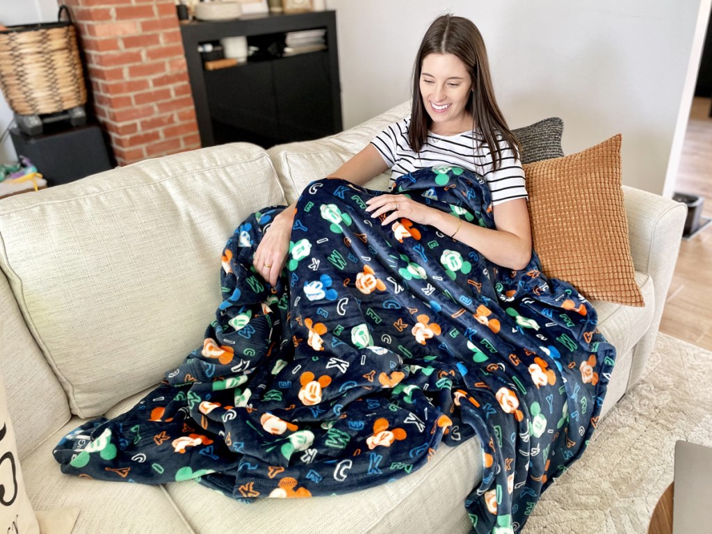 woman sitting on couch under mickey mouse print throw blanket