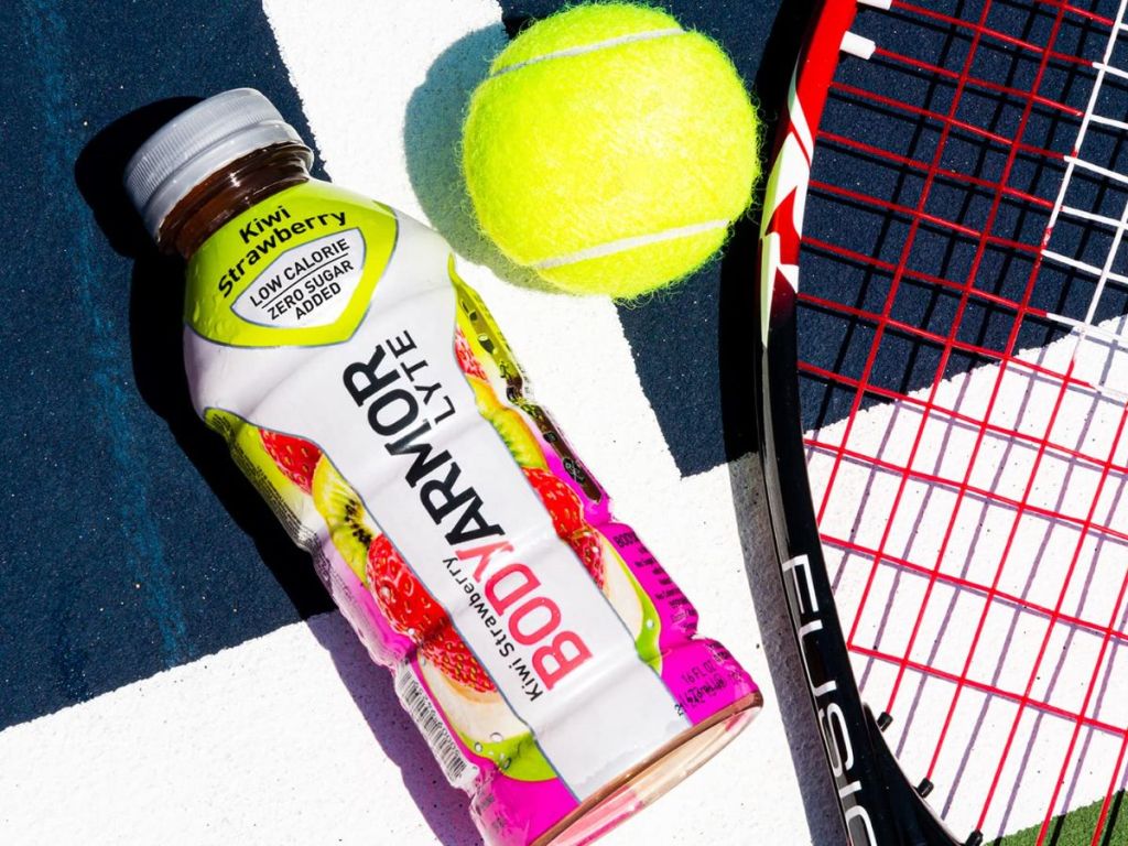 A bottle of Body Armor Kiwi Strawberry drink on a tennis court with racket and ball