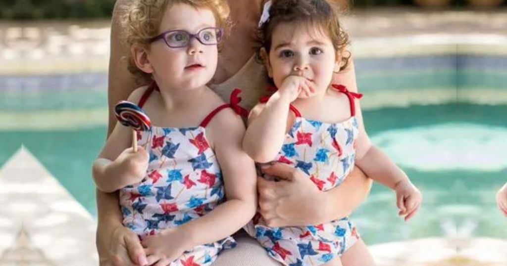 2 little girls wearing Burts Bees rompers while sitting on their moms lap