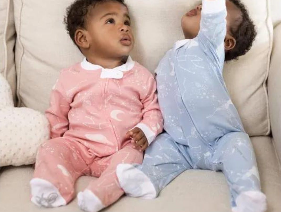 two babies sitting on a chair wearing Burt's bees 1-piece footed pajamas