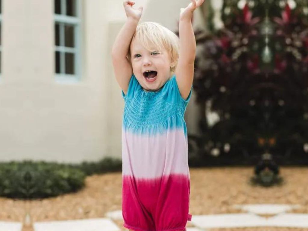 Little girl with her hands raised over her head while she is wearing a burt's bees romper