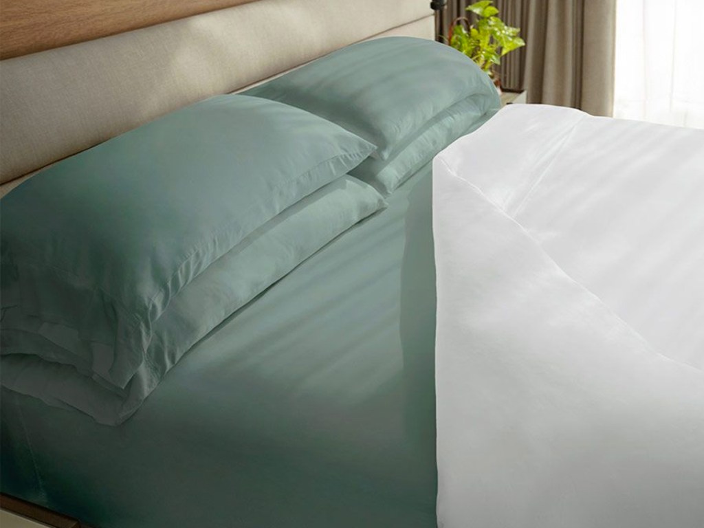 green sheet set on bed under white comforter