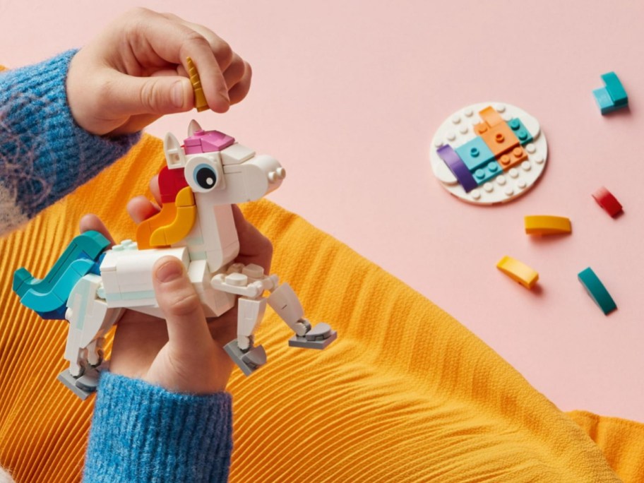 Child playing with LEGO unicorn adding its horn with multiple pieces next to her