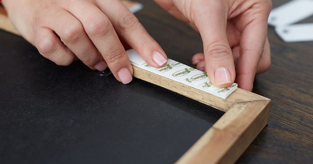 A person affixing a Command Strip to the back of a picture frame