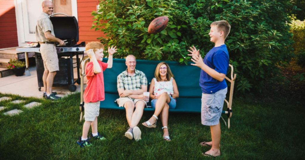 two adults sitting on a disc-o-bed set up as a couch watching two young boys play catch with a football