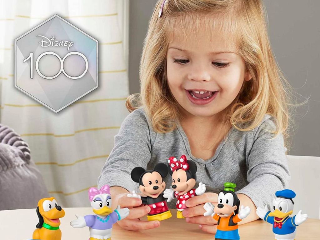 Little girl playing with small, plastic Disney character figurines. 