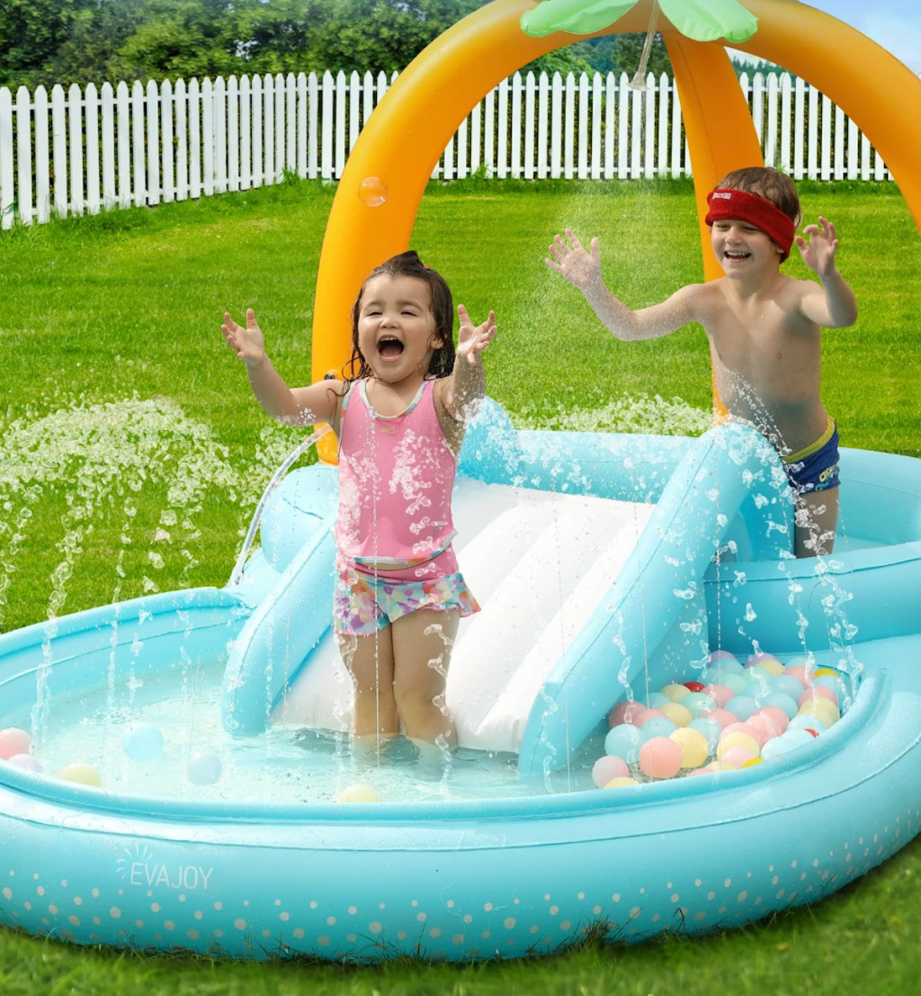 young kids playing in splash pad outside in grass with slide
