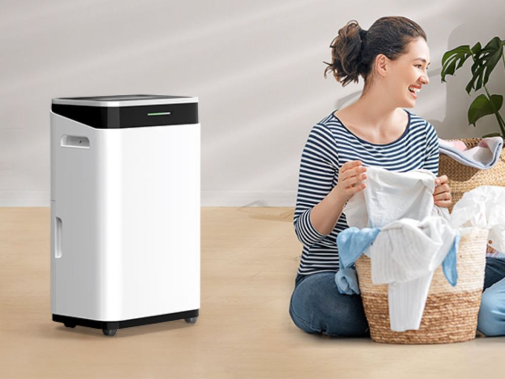 white dehumidifier on tan floor next to woman folding laundry