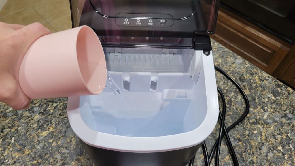 Hand pouring water from a cup into an ice maker