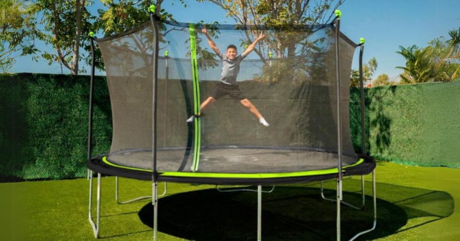 little boy jumping on a black and green trampoline with an enclosure