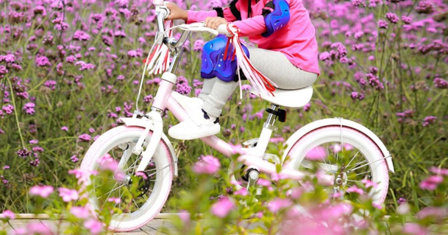 kid riding a pink and white bike with tassels and training wheels thru a bunch of pink flowers