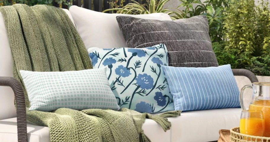 various light blue and dark grey throw pillows and green throw blanket on an outdoor bench