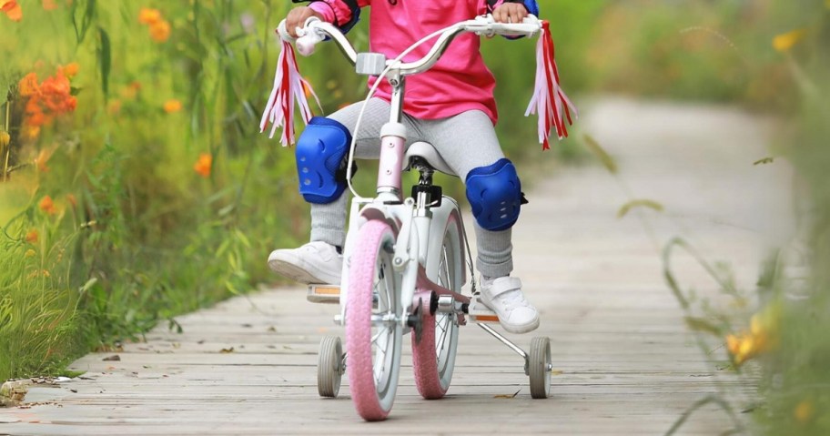 kid riding a pink and white bike with tassels and training wheels