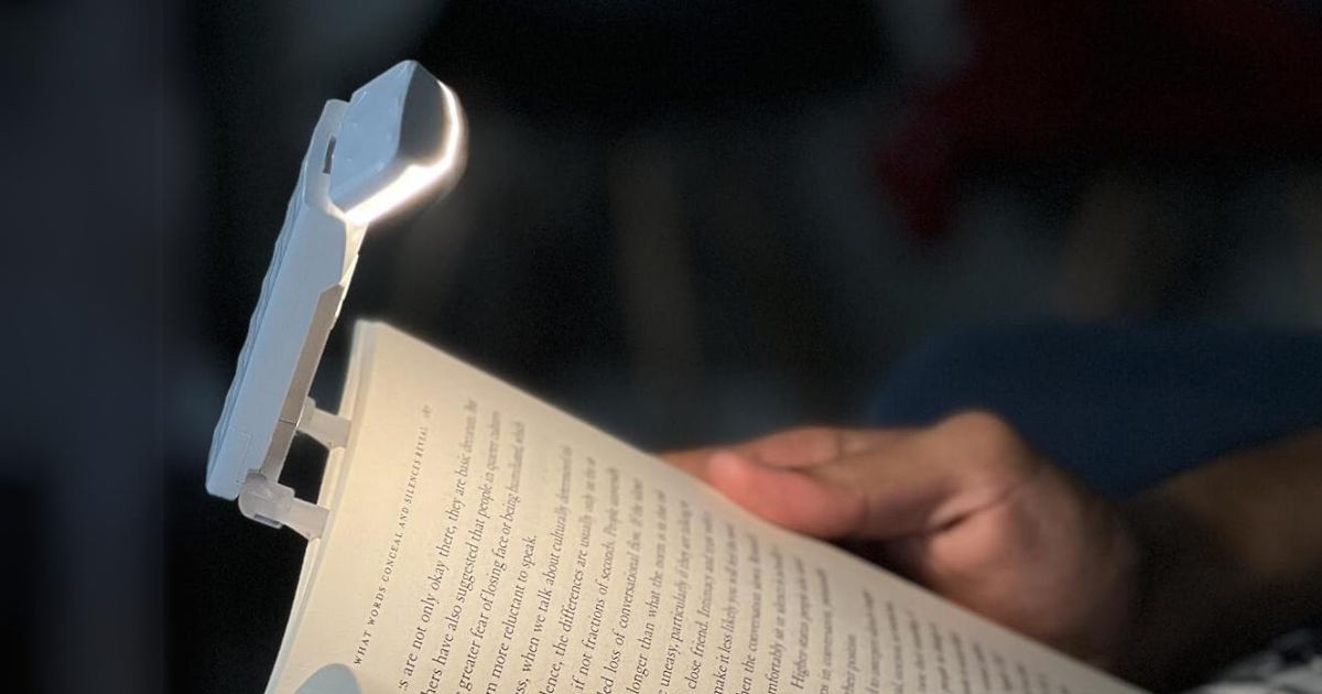 hand holding a book with a clip on book light attached shining light onto the book