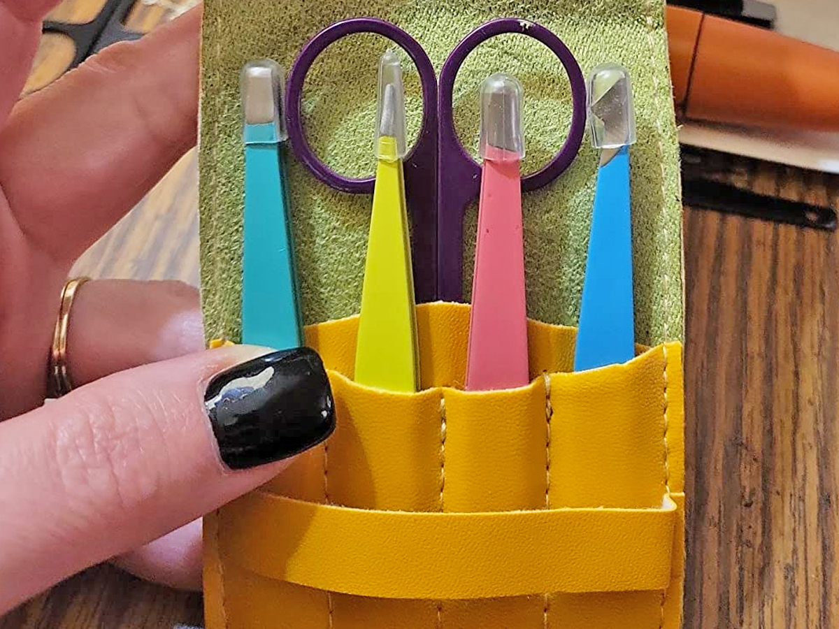 hand holding a tweezers kit with 4 tweezers and scissors