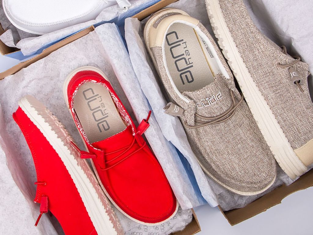 A pair of red Hey Dude shoes and a pair of tan Hey Dude shoes in their boxes
