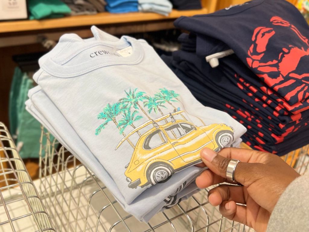 Hand holding a t-shirt with a yellow car on it and palm trees