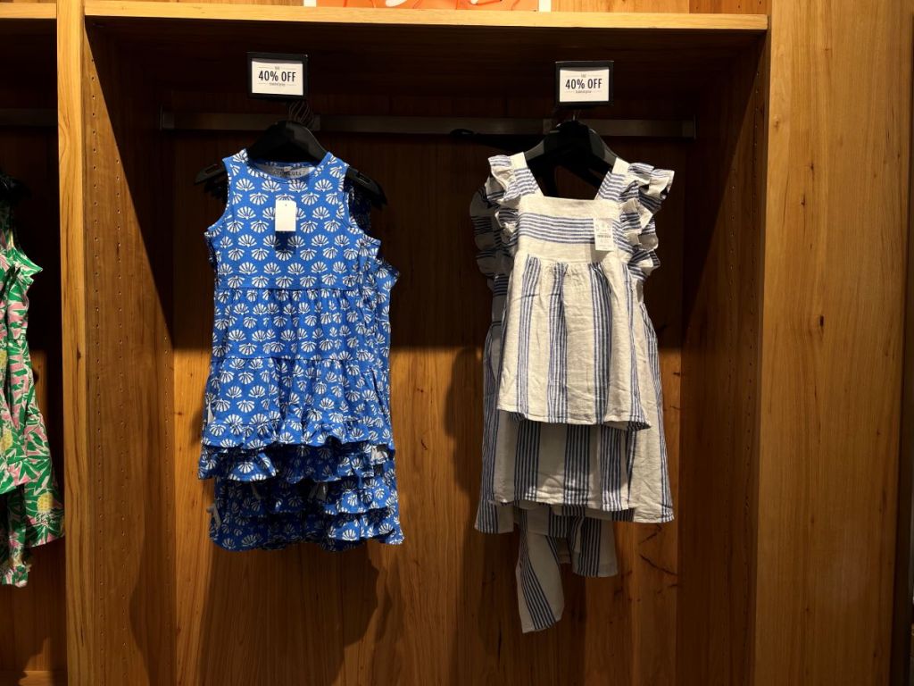 A blue dress with shells and a blue and white striped dress on hangers at a store